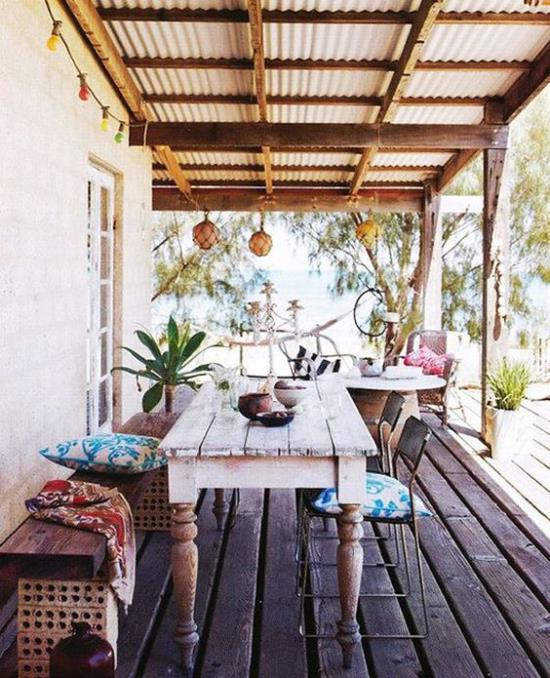 רצפת מרפסת בסגנון בוהו עשויה לוחות עץ שולחן עץ ספסל עץ כסאות מתכת ישנים כריות מושב צמחים ירוקים
