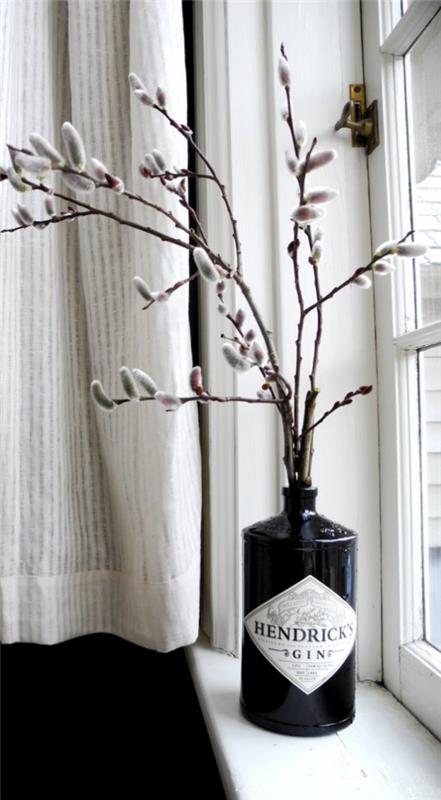 עיטור אביב עם זרדים של ערבת כוס בכלי זכוכית שחור על אדן החלון