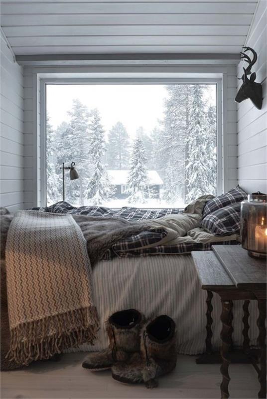 קירות זכוכית בחדר השינה. אזור שינה קטן. מיטה מול החלון. נוף חורף בחוץ