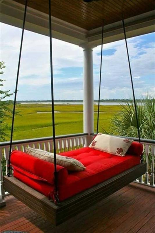 מיטה תלויה בחוץ על המרפסת המקורה, ריפוד אדום, שתי כריות נוי, נוף פנורמי נפלא של הנוף הירוק
