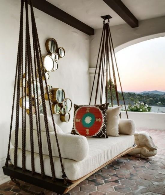 מיטה תלויה בחוץ על המרפסת המקורה בכריות בסגנון בוהו במראות עגולות כקישוט קיר