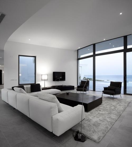 מינימליזם בסלון חדר גדול נוף יפה ספה פינתית לבנה שטיח אפור שולחן נמוך בשחור