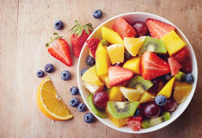 אכלו פירות בריא ירידה במשקל סלט פירות עשיר תפוזים קיווי תותים אוכמניות חתוכות לקוביות בקערה.