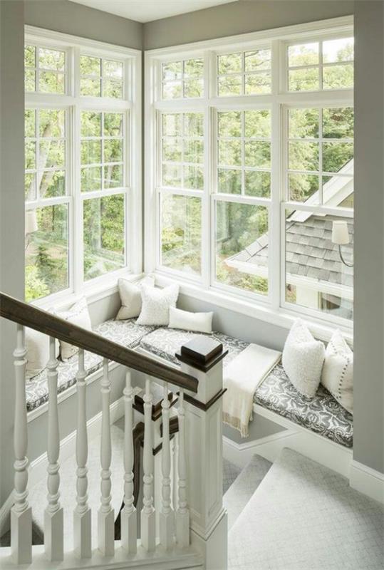 שימוש חכם בחלל בחלון הפינתי הקם פינת ישיבה נעימה בחדר המדרגות בצבע לבן ואפור