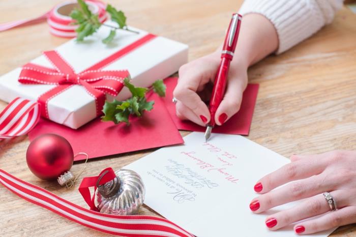 אישה צעירה כותבת כרטיסי חג המולד עם מסמרים אדומים, עט אדום וקישוטי חג